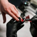 Close-up of a nail artist applying polish with precision using black gloves in a salon setting.